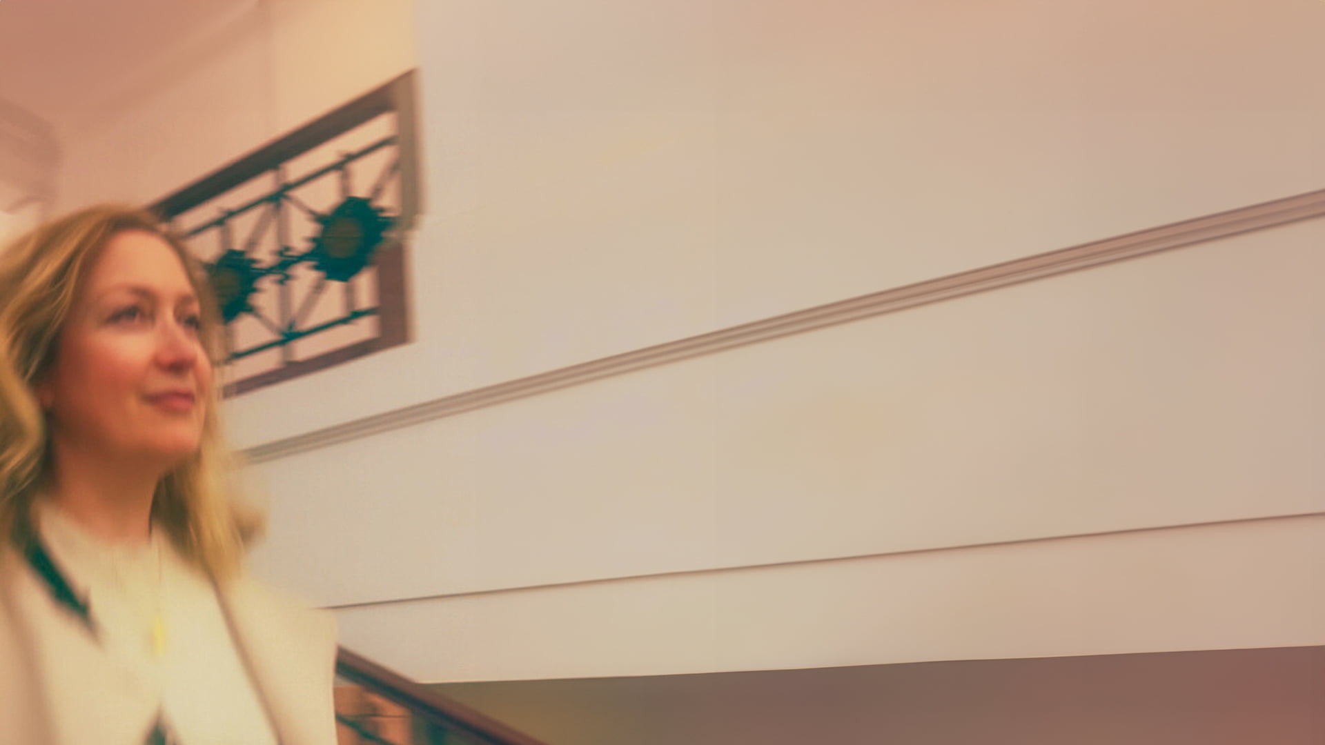 Portrait von Sandra Clemente in einem Treppenaufgang mit Bewegungsunschärfe. Sie geht die Treppe hinunter und blickt an der Kamera vorbei. Das Bild ist monochrom in Gelb- und Beigetönen.